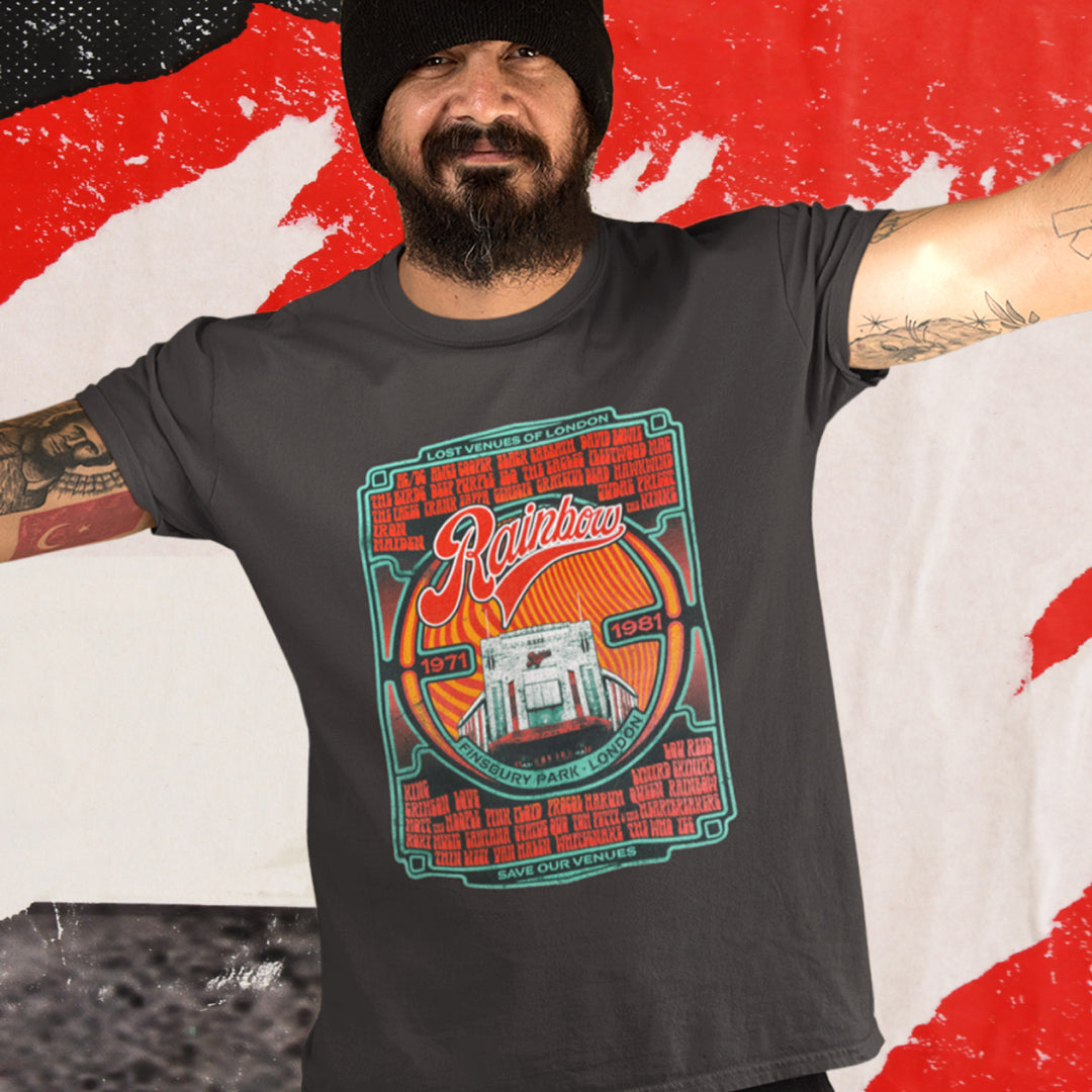 A bearded man in a black beanie and dark tee smiles, wearing the My Store Rainbow Rock T-Shirt—Limited Edition of Only 100—featuring a Rainbow Theatre Retrospective (1971-1981) and iconic London venue art on a red and white background.
